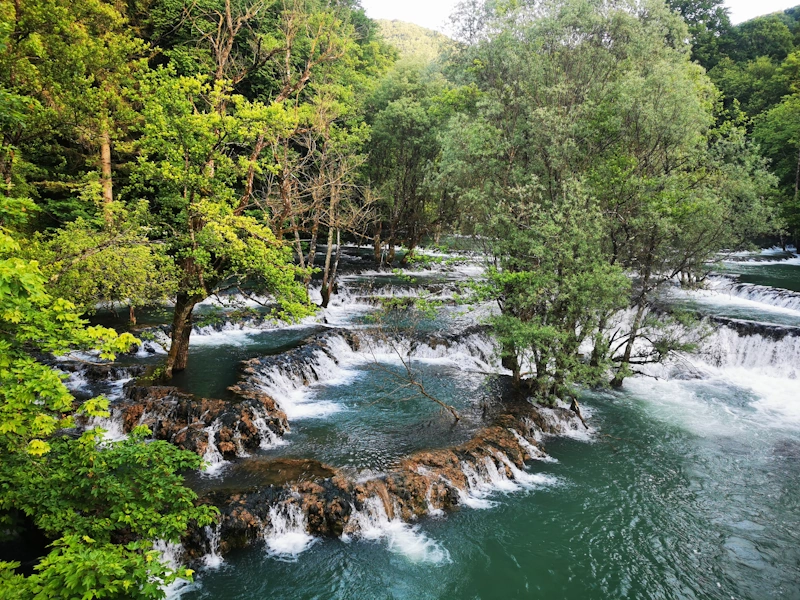Fahrer und Motorräder vor den beeindruckenden Una‑Wasserfällen