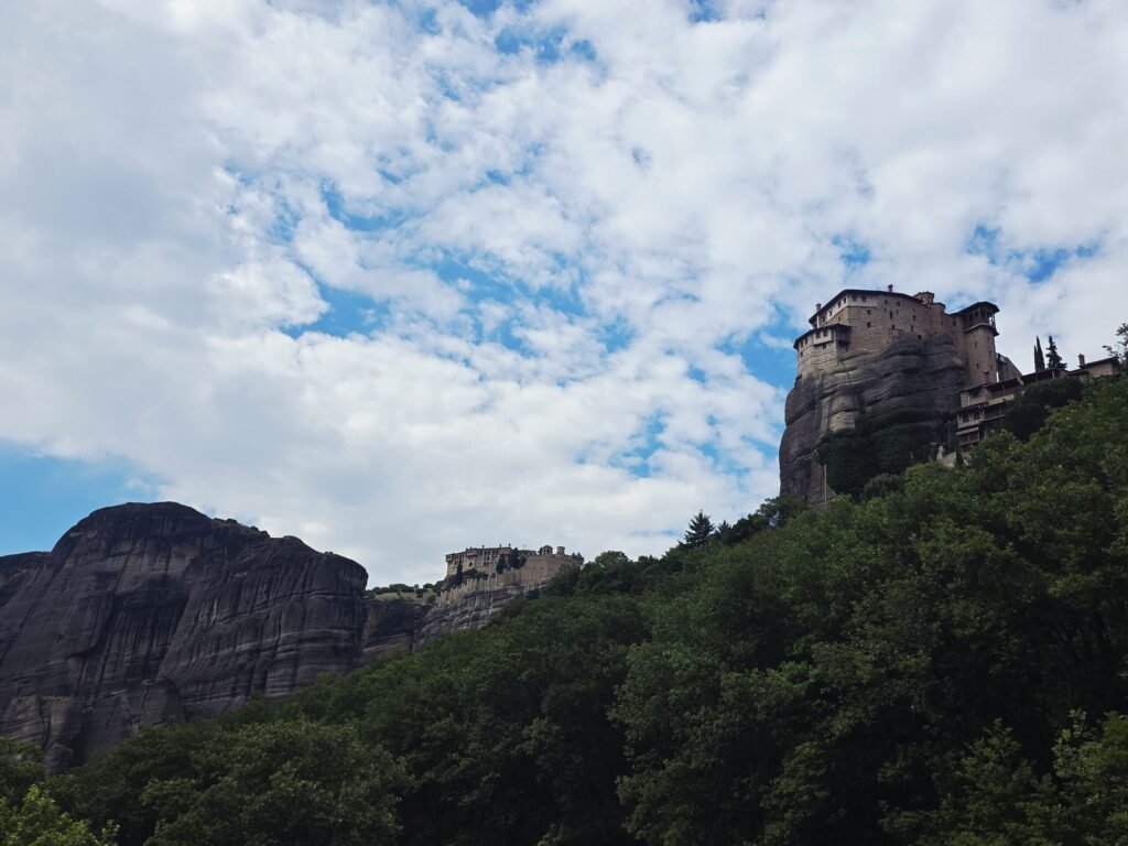 Biker auf kurviger Bergstraße vor den historischen Meteora‑Klöstern in Zentralgriechenland.