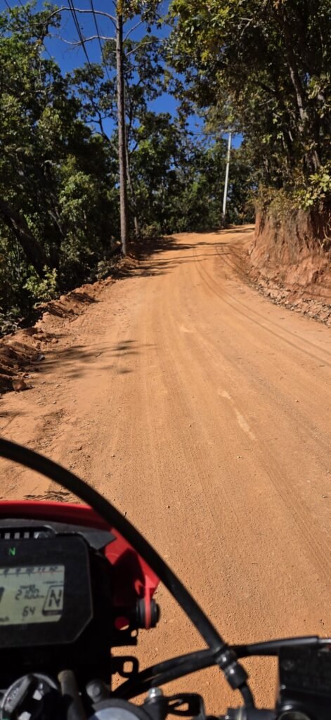 Motorrad auf einer unbefestigten Offroad‑Route nahe Pai – rote Erde und dichter Dschungel